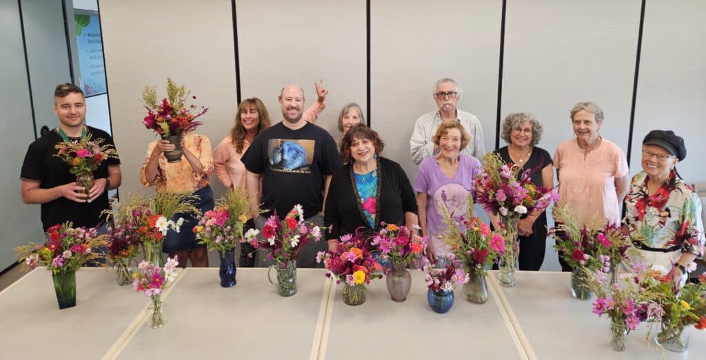 A group of people standing behind a table with flower arrangements in vases