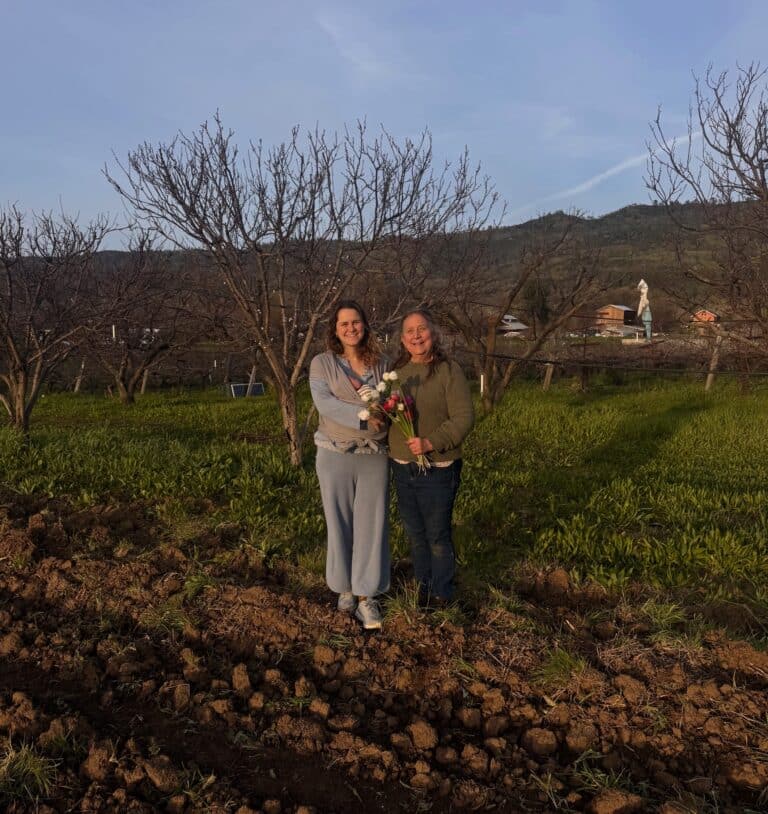 Hannah and Dru at the edge of the field. Hannah is holding a baby.